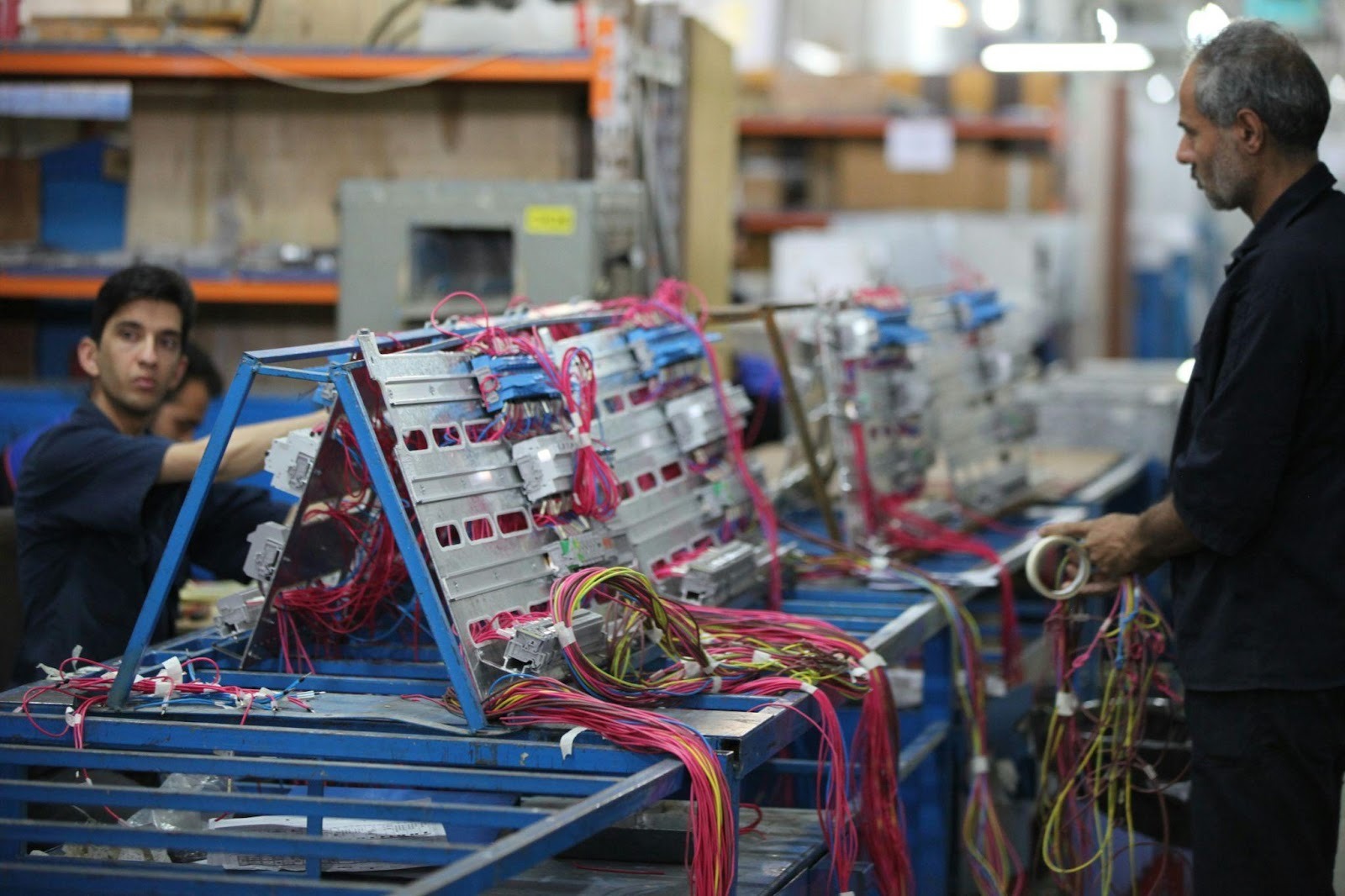 Technicians assembling electric motor components with colorful wiring on an industrial production line inside a manufacturing facility.