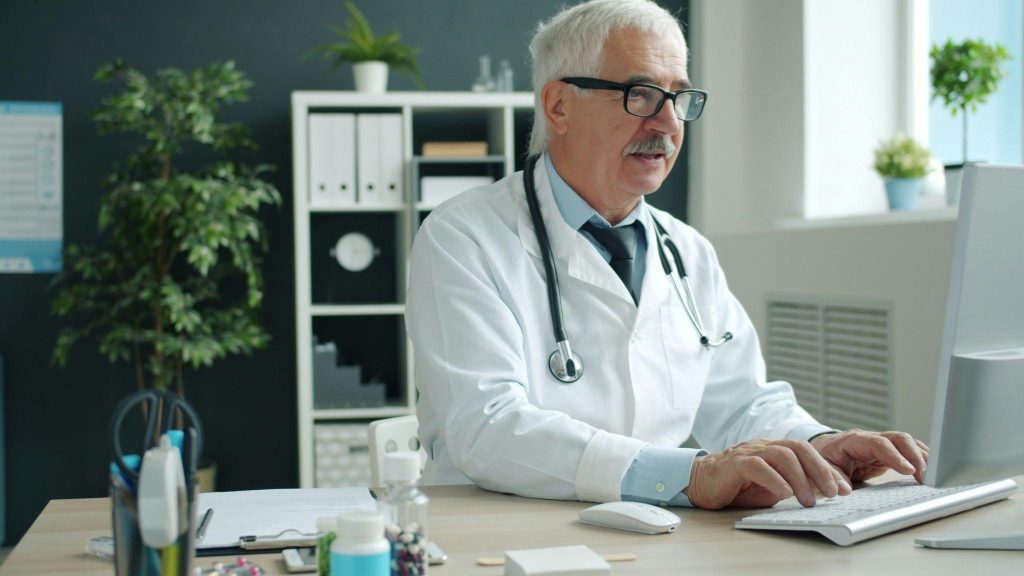 Physician typing at his computer, sending patient records securely through an EMR fax connection.
